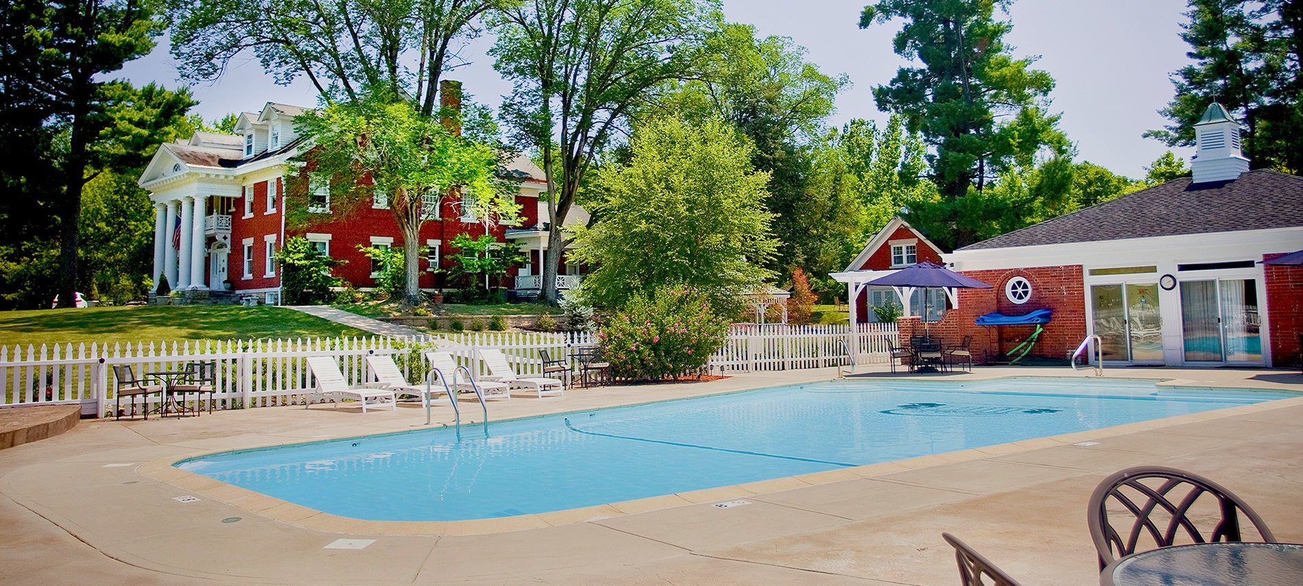 A crystal blue swimming pool in the foreground with a red brick mansion in the background
