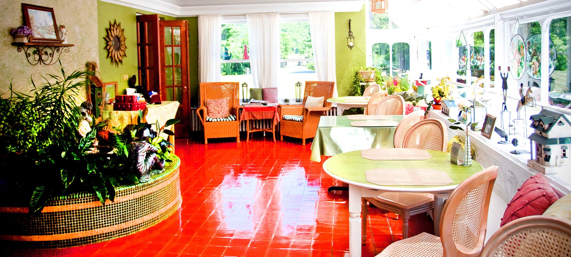 A brightly lit sunroom with red slate floor and two green tables to the right