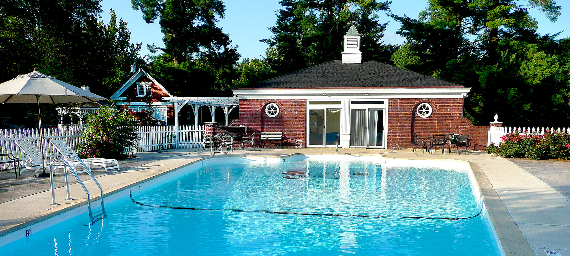 A swimming pool with red brick pool house in the background
