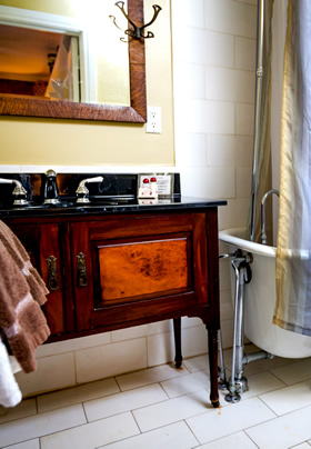 An antique wooden bathroom vanity with black marble top and partial view of a clawfoot tub