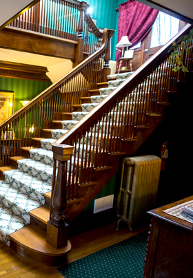 A grand wooden staircase from the side, with white and green patterned carpeting on the stairs