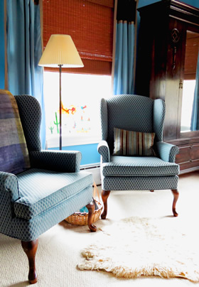 Two blue wingback chairs in front of a window with a tall lamp standing between
