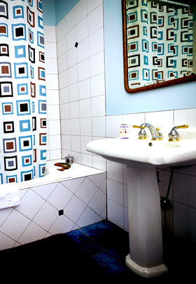 A white pedestal sink to the right with a white tiled jacuzzi tub to the left with a blue, brown and black pattered shower curtain