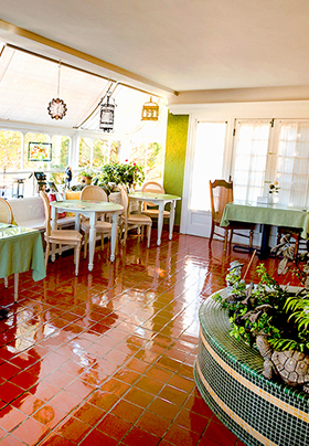Brightly lit sunroom with red slate tile, dining tables along the walls and a fountain base to the right